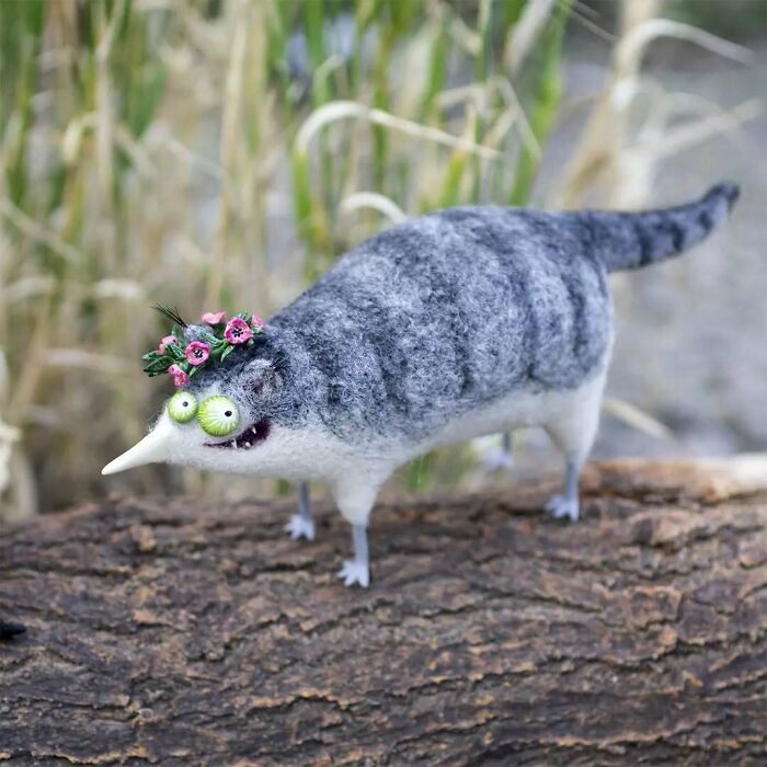 Strange art doll resembling a funny-looking animal with a floral wreath, created by a Georgian artist, on a log.