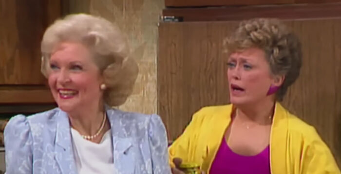 Two women from a popular comedy show scene in the kitchen, one wearing a blue suit and the other in a yellow jacket.