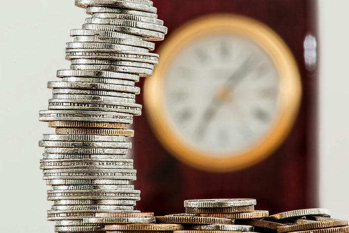 A stack of coins in front of a blurred clock, symbolizing quality life hacks related to time and money management.