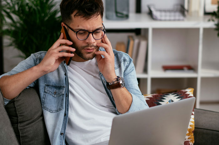 Man in glasses on phone call, typing on laptop, discussing corrupt actions by officers.