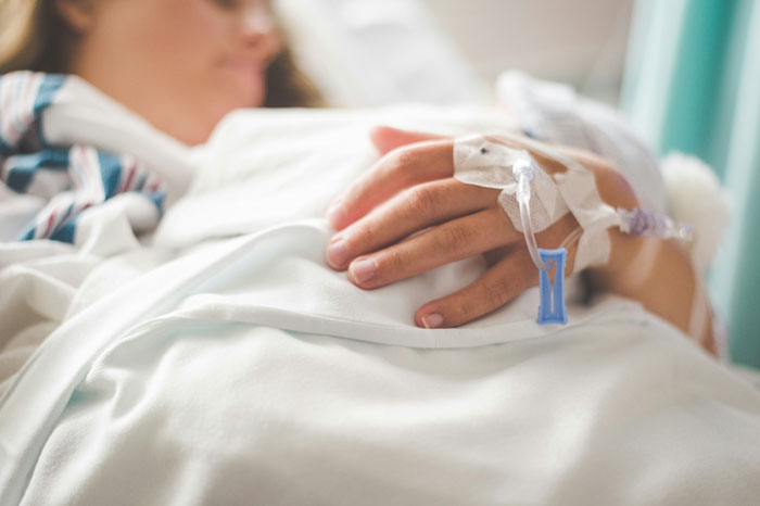 Person resting in hospital bed with IV in hand, possibly reflecting a family's untold story.