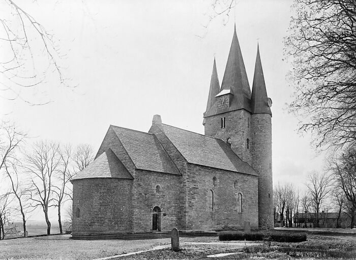 Historic stone church with tall spires, surrounded by bare trees under a cloudy sky; fascinating architecture.