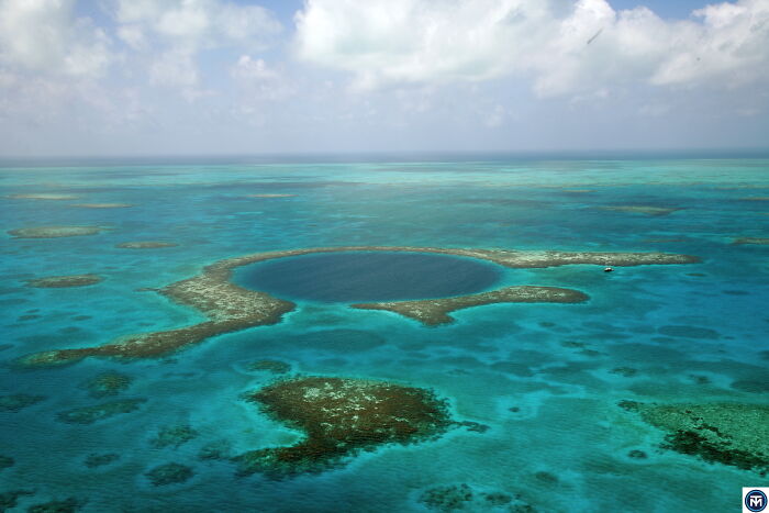 Aerial view of a stunning natural phenomenon, the Great Blue Hole surrounded by turquoise ocean waters under a cloudy sky.