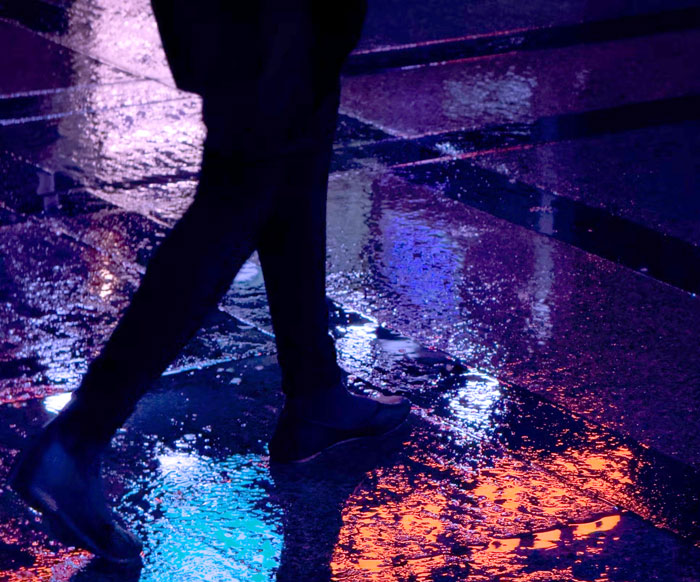 Person walking on a wet city street at night, reflecting urban lights, evoking mystery like true crime cases.