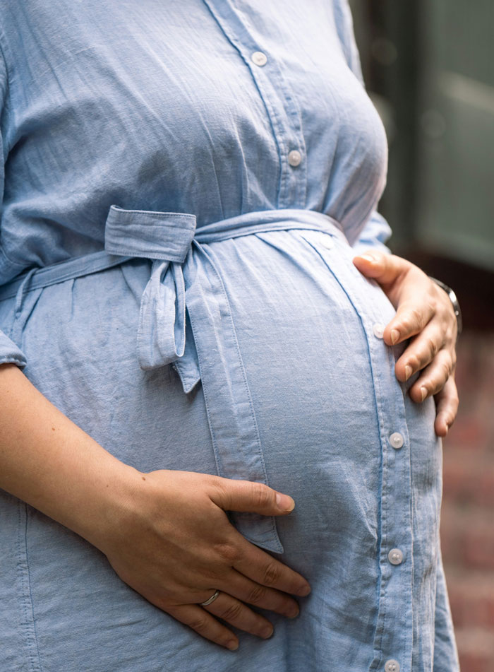 Pregnant woman in a light blue dress holding her belly, representing a family story theme.