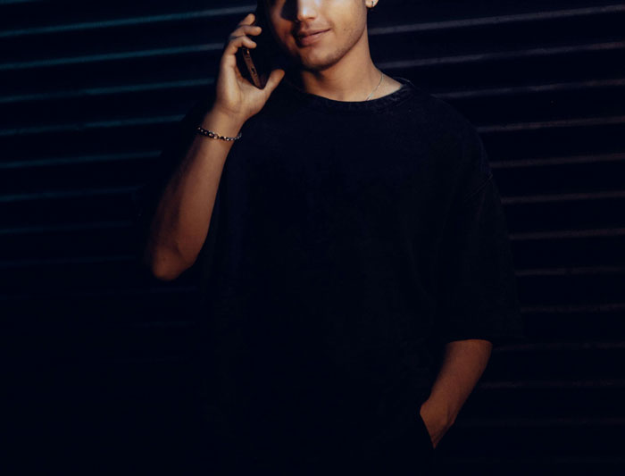 Young man on a phone call, partially lit, representing the unsolved mysteries theme in true crime cold cases.