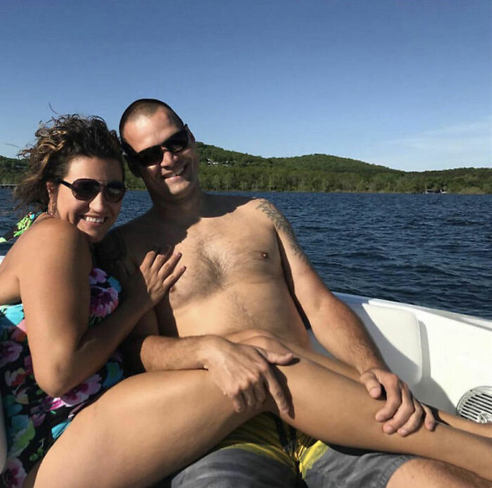 A couple on a boat with confusing perspective, creating an optical illusion against a scenic water backdrop.