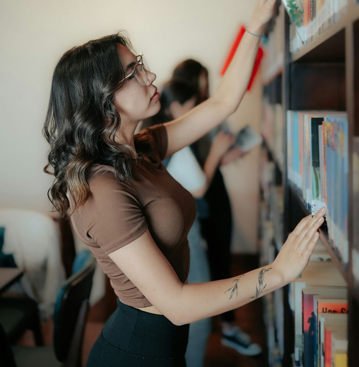 Young woman searching for books on a library shelf, illustrating quality hacks in everyday life.