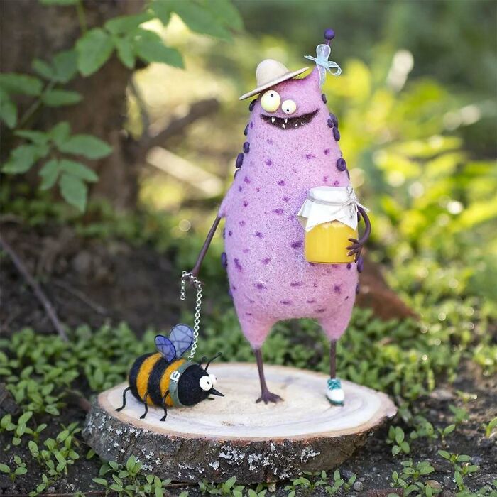 Strange art doll by Georgian artist holding a jar, with a bee on a leash, on a wooden slice in a garden setting.