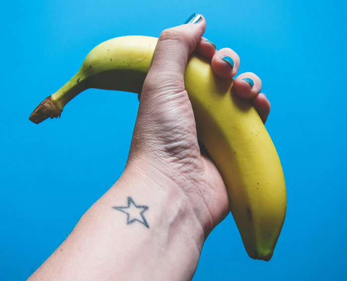 Hand holding a banana against a blue background, showcasing quality life hacks with a star tattoo visible on the wrist.