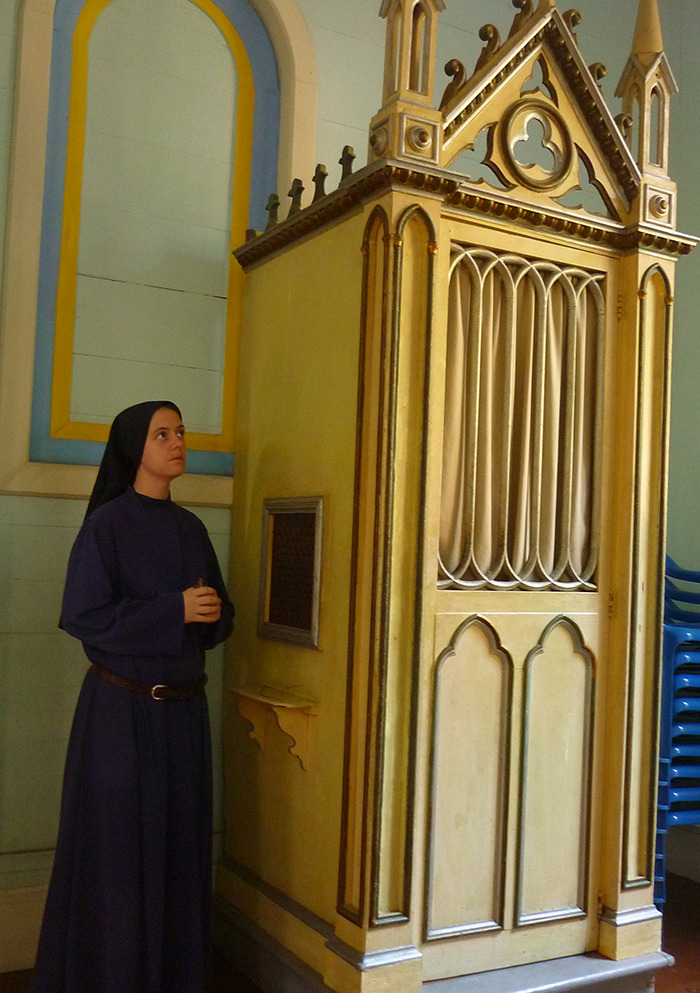 Nun in traditional habit standing by an ornate confessional, symbolizing a spiritual journey from the spotlight. 