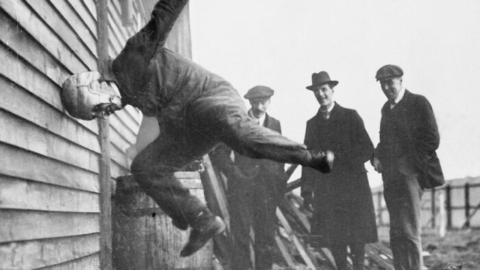 Man testing an early helmet invention while others observe, showcasing a historical invention ahead of its time.