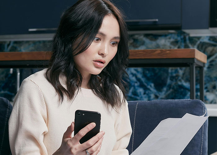 Woman looking shocked, holding a phone and paper, related to trust fund distress.