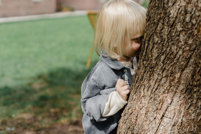 Child hiding behind a tree, representing family secrets and untold stories.