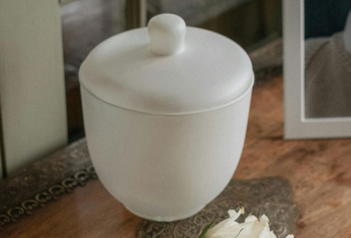 A white ceramic urn on a wooden table beside a framed photo, symbolizing unsolved true crime cold cases.