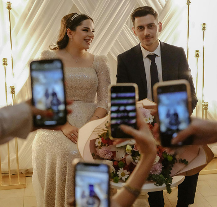 Bride and influencer at a ceremony, surrounded by people holding smartphones, capturing the moment.