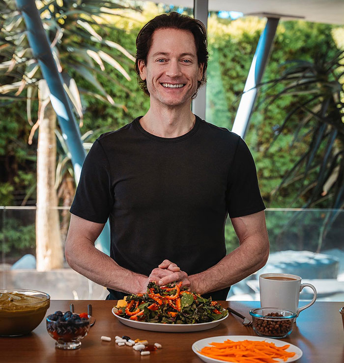 Billionaire in a casual setting, smiling with a healthy meal, coffee, and supplements, symbolizing efforts to reverse aging.