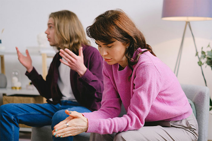 Woman in pink sweater appears upset, sitting apart from a man gesturing behind her, highlighting betrayal theme.