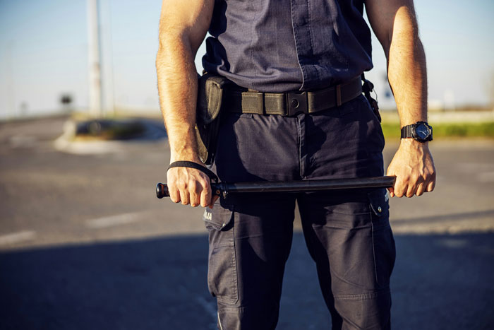 Officer standing in uniform holding a baton on a deserted road.