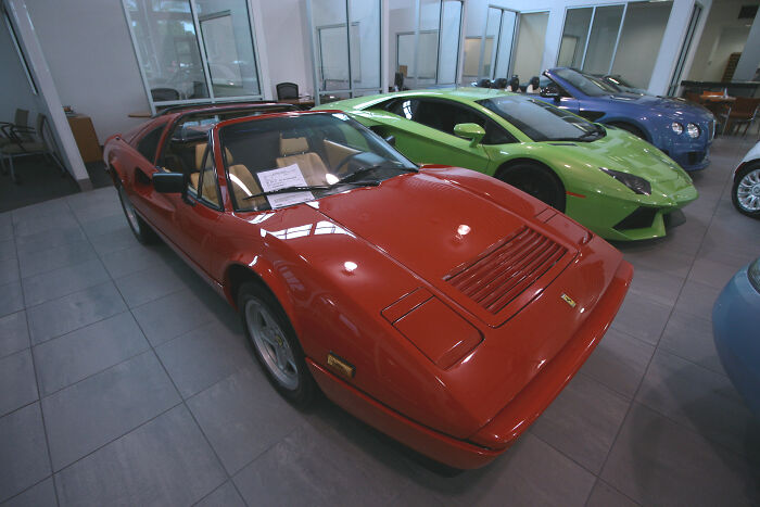 Red 80s sports car alongside modern models in a showroom, evoking nostalgia for classic automotive design.