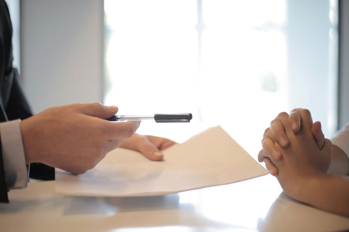 Doctor holding documents and pen, discussing with hands-folded person in bright room, highlighting insurance concerns.