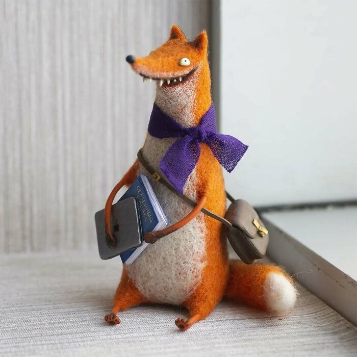 Funny-looking animal art doll with a purple scarf, carrying books and a bag, created by a Georgian artist.