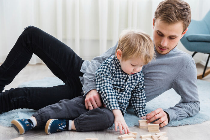 Father and young child playing with blocks on the floor, highlighting the innocence of childhood before realizing complex issues.