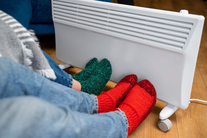 Middle class warming feet by heater with colorful socks, highlighting heating costs.