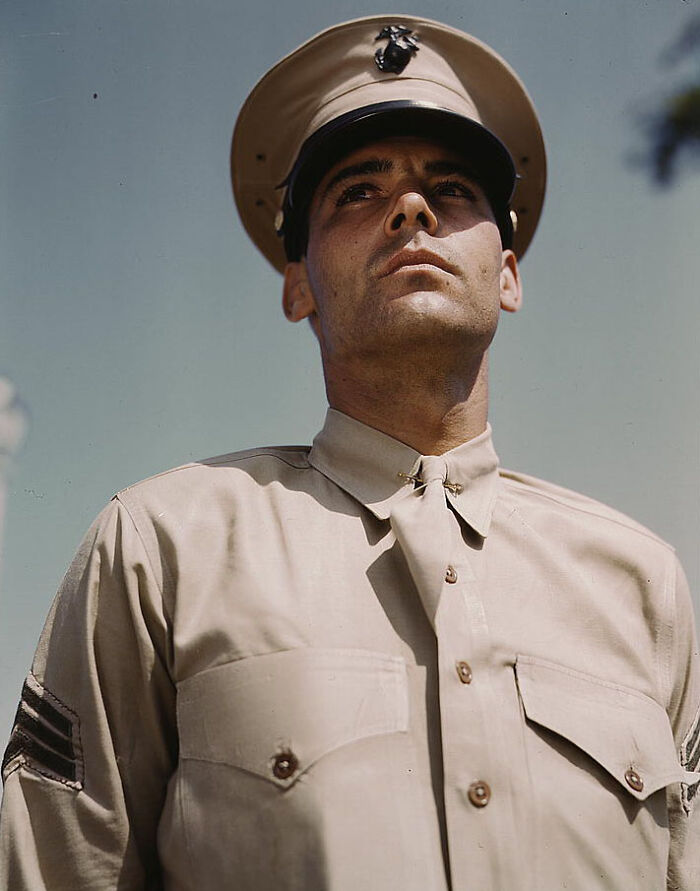 Marine in 1940 color photo wearing a uniform with a cap, gazing upward against a clear blue sky.