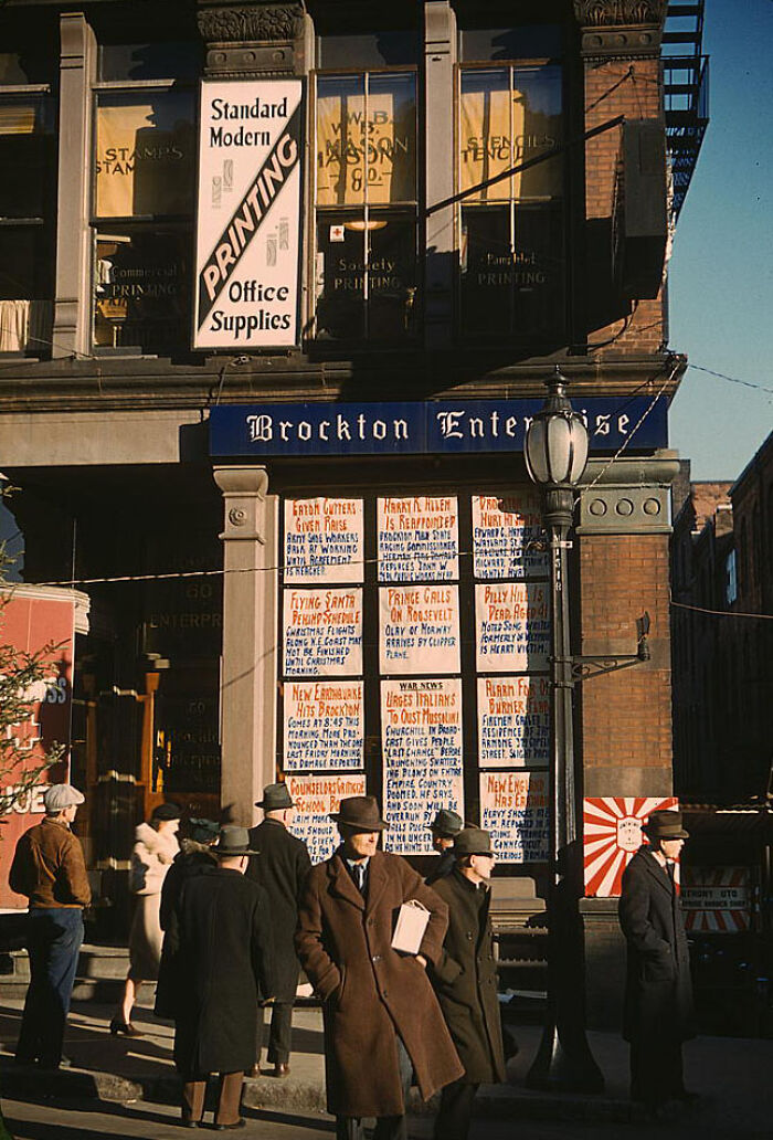 1940 color photo of people in coats and hats outside a Brockton Enterprise storefront displaying news headlines.