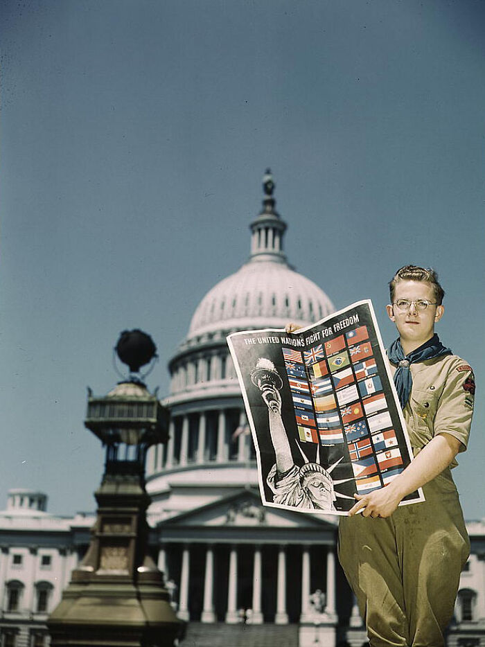 Boy in scout uniform holding a "Fight for Freedom" poster in front of the Capitol building, 1940 color photo.