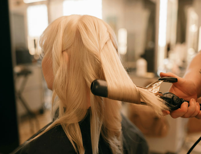 Woman having her hair styled with a curling iron in a salon setting.