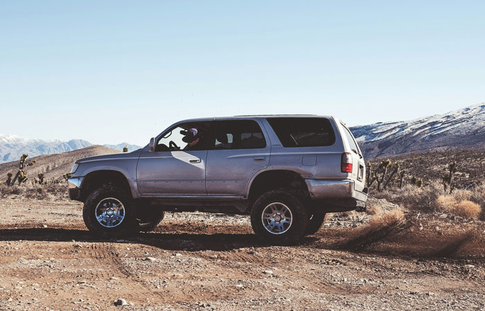 Silver SUV driving through a desert landscape, evoking unsatisfied feelings from true crime cold case enthusiasts.