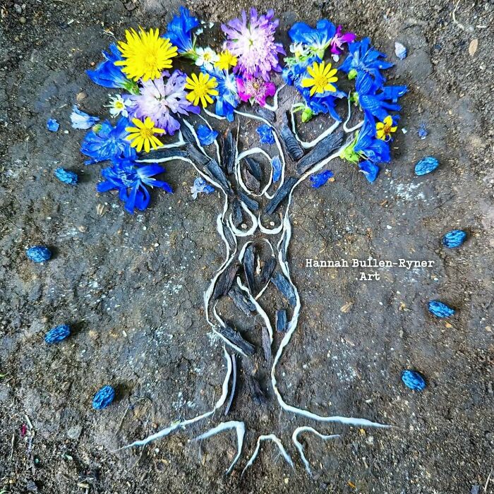 Earth art depicting a tree with a human form, created using colorful natural materials like flowers and twigs.