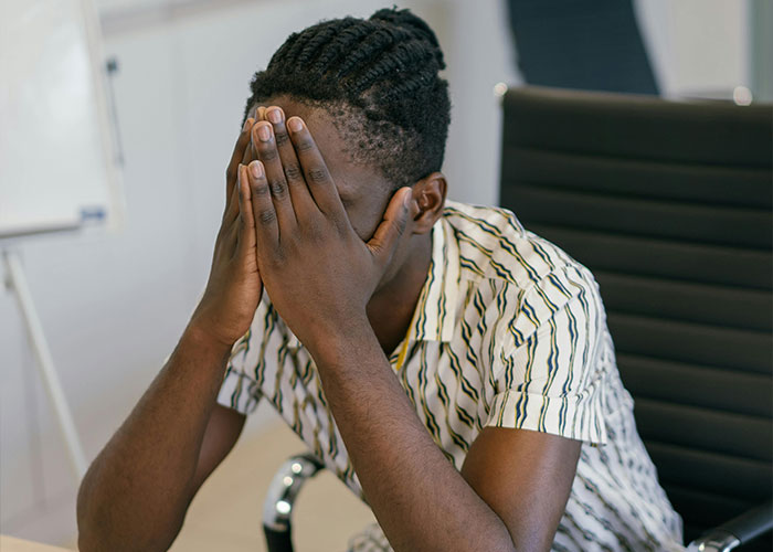 Person in a striped shirt sitting at a desk, covering their face, possibly experiencing an awkward job interview moment.