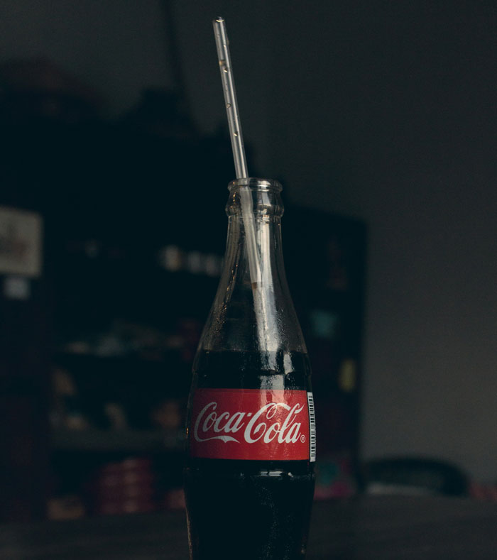 A glass Coca-Cola bottle with a straw, showcasing a quality hack for sipping drinks easily.