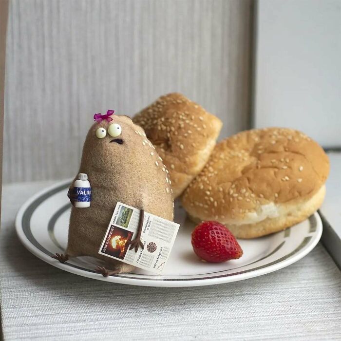 Funny-looking animal doll by Georgian artist on a plate with buns and a strawberry, holding a tiny bottle and newspaper.