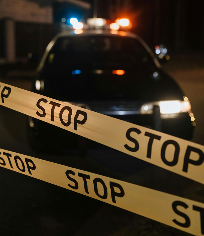 Police car with lights flashing behind crime scene tape, highlighting true crime and unsolved cold cases.