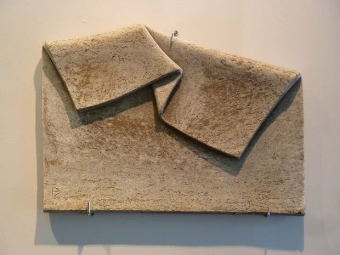 A sculpture resembling a folded blanket, defying physics, crafted from stone.