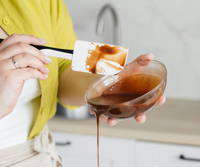 Person holding a bowl of chocolate sauce with a spatula, symbolizing untold family stories in the kitchen.