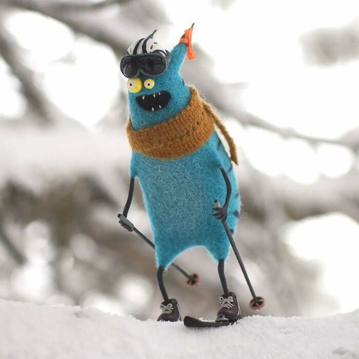 Strange art doll, a funny-looking blue creature skiing with goggles and a scarf, in a snowy setting.