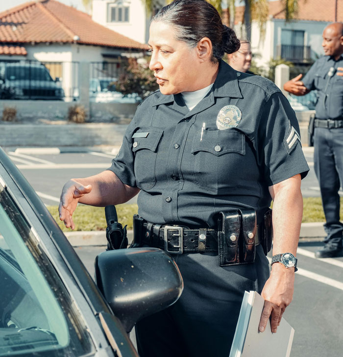 Police officer in uniform stands by a car, engaging in conversation, reflecting real-life quality hacks in community policing.