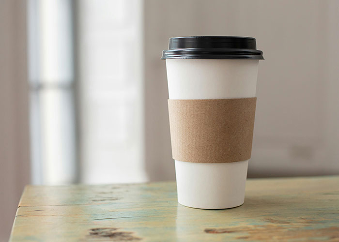 Disposable coffee cup with a black lid on a rustic table, symbolizing awkward job interviews theme.