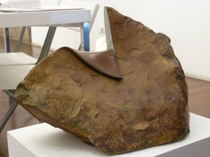 A realistic sculpture resembling soft leather draped over a stone, displayed in a modern gallery setting.