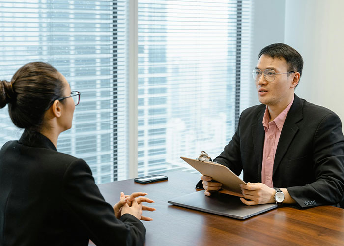 Two people in a professional setting, one holding a clipboard, engaged in a job interview discussion.