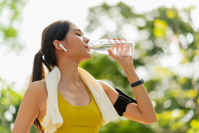 Woman in workout gear with earbuds drinking water, embodying quality life hacks.