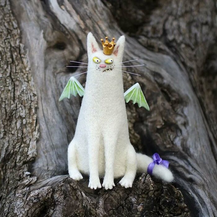 Strange art doll resembling a feline with a crown and wings, on a textured wooden background.