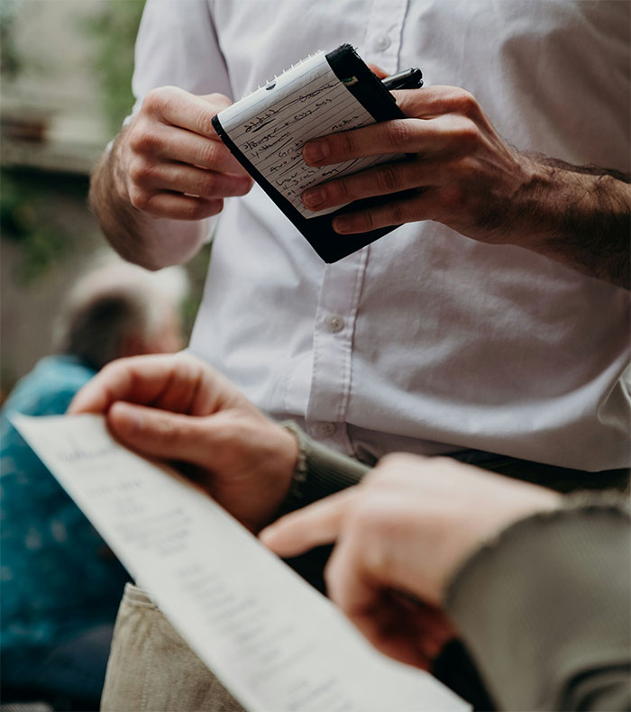 Person in white shirt writing an order, while another hand holds a restaurant menu, focusing on paying for dinner.