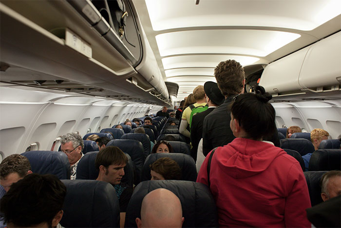 Passengers deplaning row by row from an airplane cabin, following instructions.