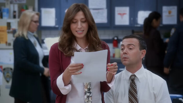 Two characters in an office setting, with one reading a paper aloud, representing a beloved TV show scene.